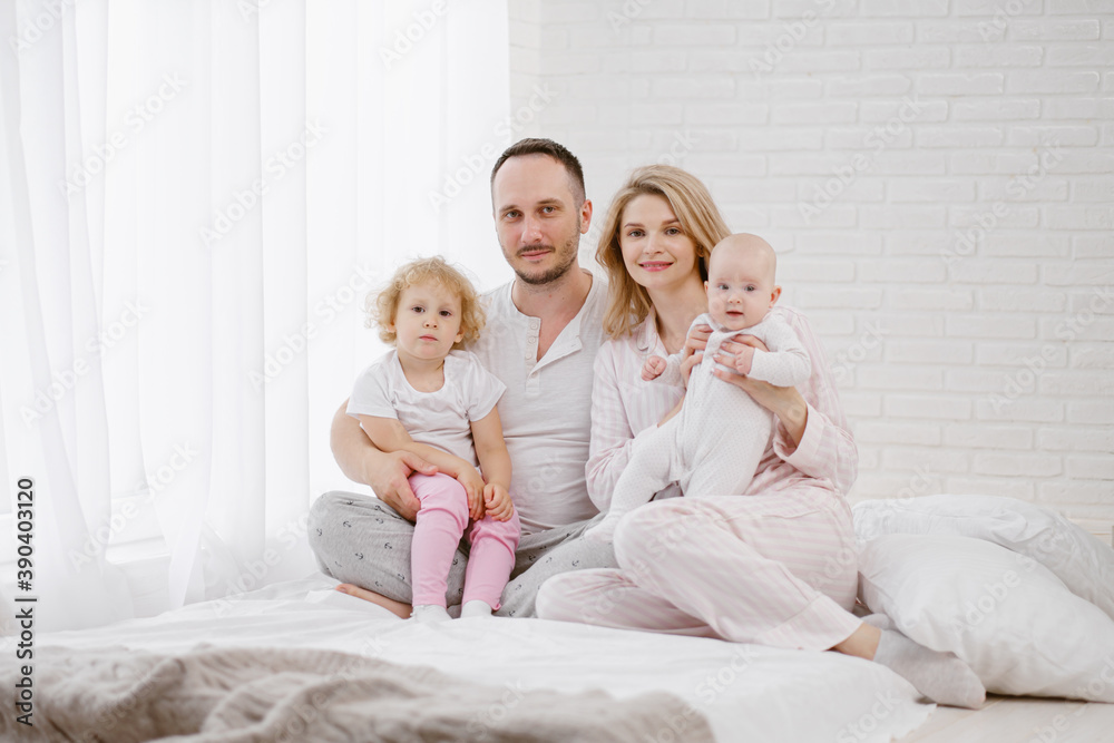 A young Caucasian family with two children daughters in a white home interior. Home clothes.