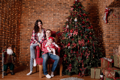 Happy family at Christmas eve sitting together near decorated tree at living room, home. Father, mother and baby girl. Concept of celebrating New Year holiday © Andriy Medvediuk