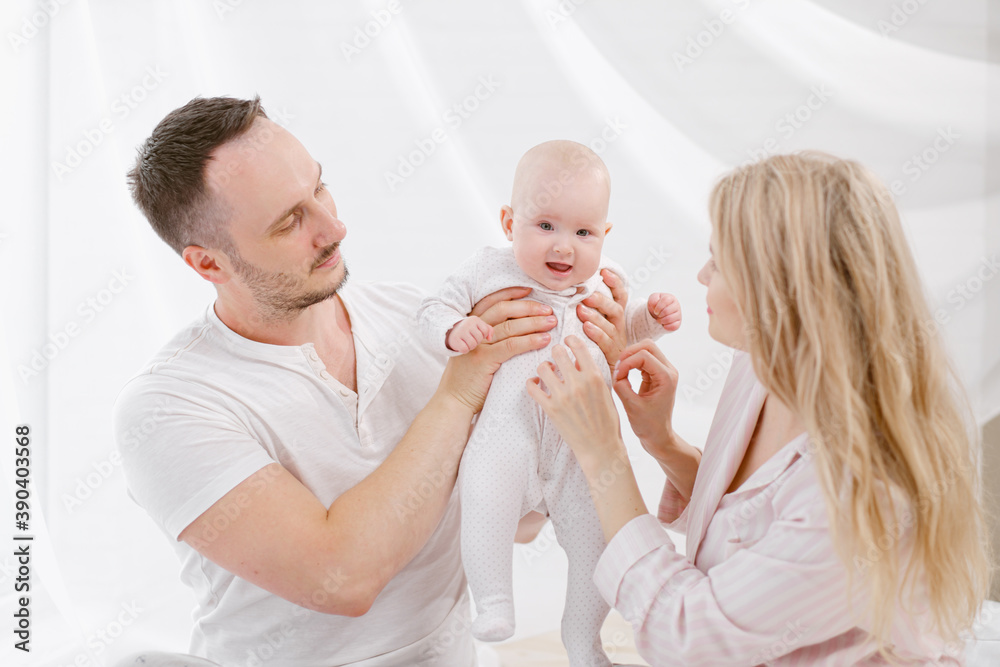 A young Caucasian family with a newborn baby daughter in the bedroom. White light home interior. A young Caucasian family with a newborn baby daughter in the bedroom. White light home interior.
