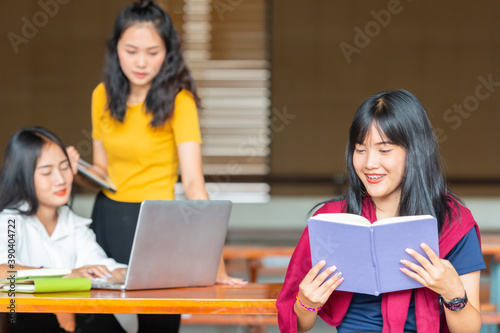 Female asian student outdoors holding book and smiling  and Background blur University students doing group study. © shine