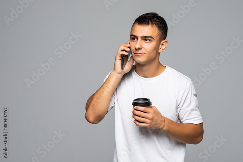 Portrait of happy man talking on phone and drinking coffee isolated on gray background © dianagrytsku