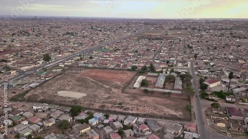 Aerial flyover of large expansive  South African township with small RDP houses and dusty school grounds at sunset.