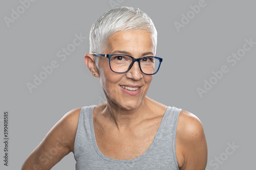 Foto Smiling senior woman with short white hair and glasses posing in front of gray b