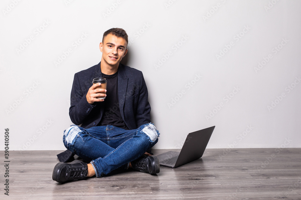 Young man working on laptop sitting on floor reading news, surfing net or freelancing isolated on white background