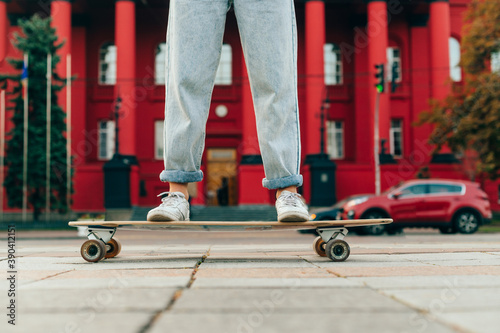 Close photo of woman's legs in jeans and sneakers rides on a longboard on a background of red architecture. Background. Skate concept. photo