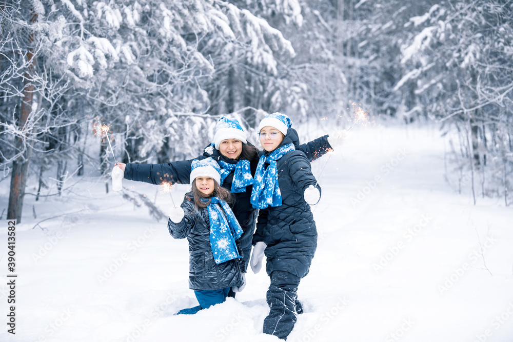 Smiling young girls and there mother with sparklers in hands. Happy winter time in the forest. The girls are in a dark coat,  blue  Santa Claus hat, scarf and mittens. Family christmas new year.