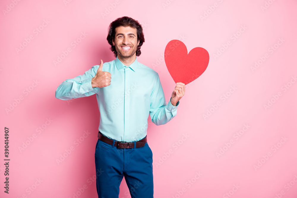 Photo portrait of man holding red heart card showing thumb up isolated on pastel pink colored background Photo portrait of man holding red heart card showing thumb up isolated on pastel pink colored background