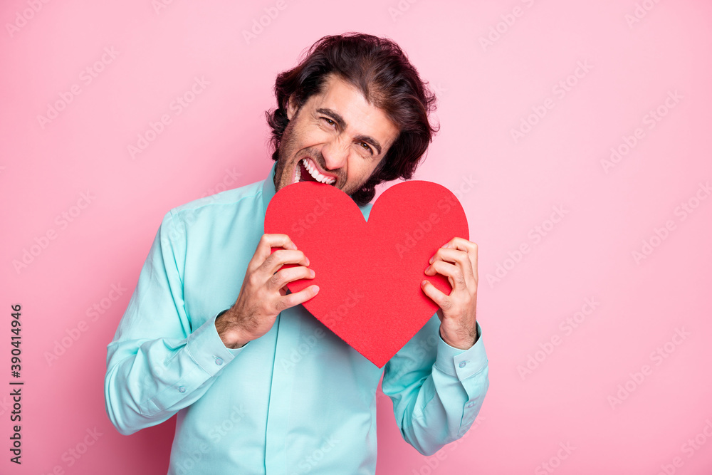 Photo portrait of guy biting big red heart card isolated on pastel pink colored background Photo portrait of guy biting big red heart card isolated on pastel pink colored background