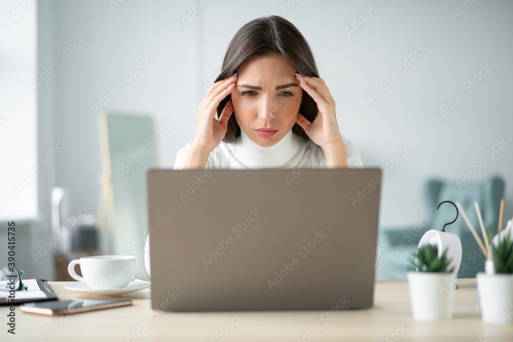 Frustrated young woman sits in front of a laptop screen and keeps her hands on her temples in a light office. Frustrated young woman sits in front of a laptop screen and keeps her hands on her temples in a light office.
