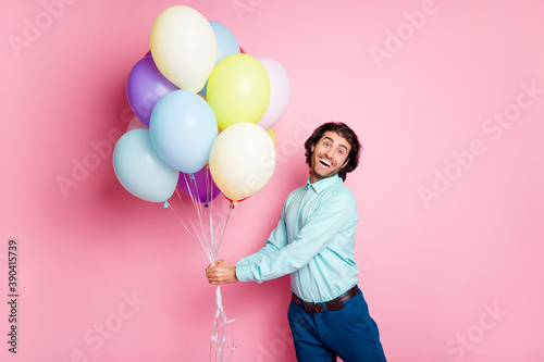 Photo portrait of glad guy holding air balloons with two hands isolated on pastel pink colored background