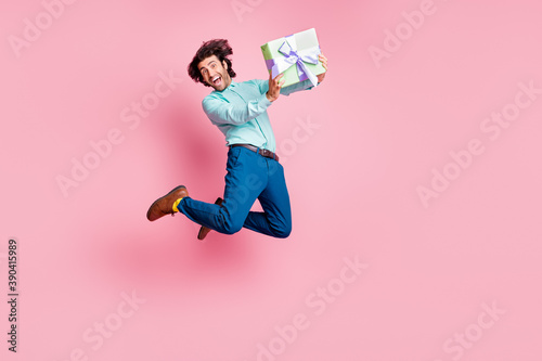 Full length photo portrait of happy man holding wrapped present box jumping up isolated on pastel pink colored background