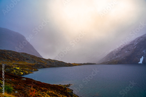 Dramatic storm clouds with bright sunlight breaking through. High mountain plateau with a clear blue lake.
