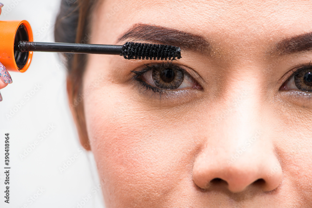 Asian woman applying mascara on eyelashes with makeup brush in the morning time. Advertising concept