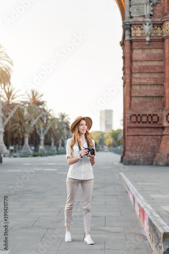 Female solo traveler holding a vintage camera while walking around the city of Barcelona in a nice outfit with a hat. Amateur photographer enjoying taking pictures