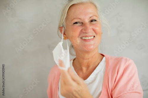 Portrait of senior woman taking off protective medical mask for protection from virus