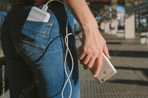 Power Bank in the girl's back pocket and a smartphone in her hand, against the background of the station.
