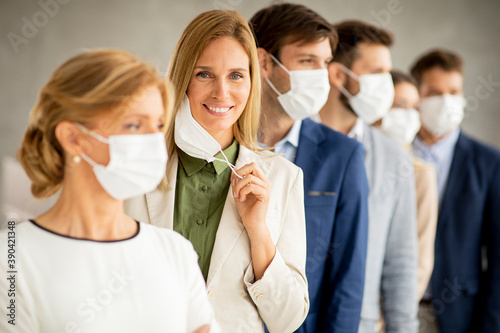 Business woman taking off her protective facial mask and looking at the camera with her team members standing in the line
