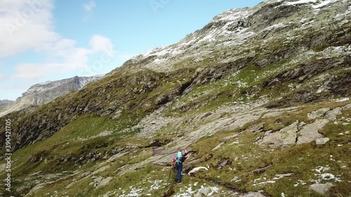 A woman in pink jacket hiking in the Hohe Tauern region in Austria. The slopes are partially covered with snow. Upper parts steep and sharp. Early spring in the Alps. Serenity and calmness.
 photo