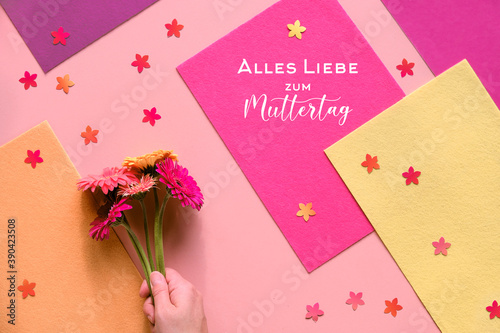 Text Alles Liebe zum Muttertag means Much love for Mother's day. Flat lay with hand, gerbera flowers © tilialucida