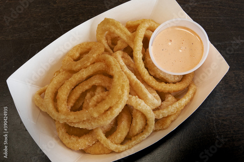 Deep fried onion rings in a take out tray with dipping sauce