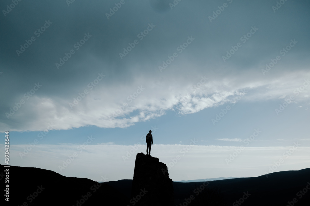 dark silhouette of a man standing on a mountain against a sky partially covered by a cloud