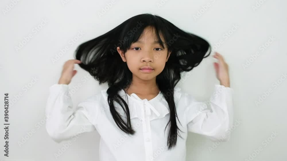 Asian child girl turned around and her hand over her long, swaying hair and a bright smile on a white background, slow motion Asian child girl turned around and her hand over her long, swaying hair and a bright smile on a white background, slow motion