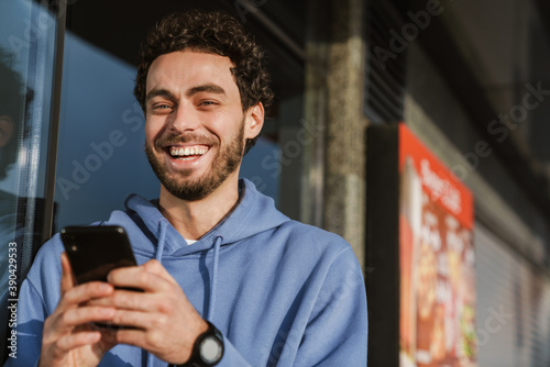 Happy handsome guy smiling and using mobile phone