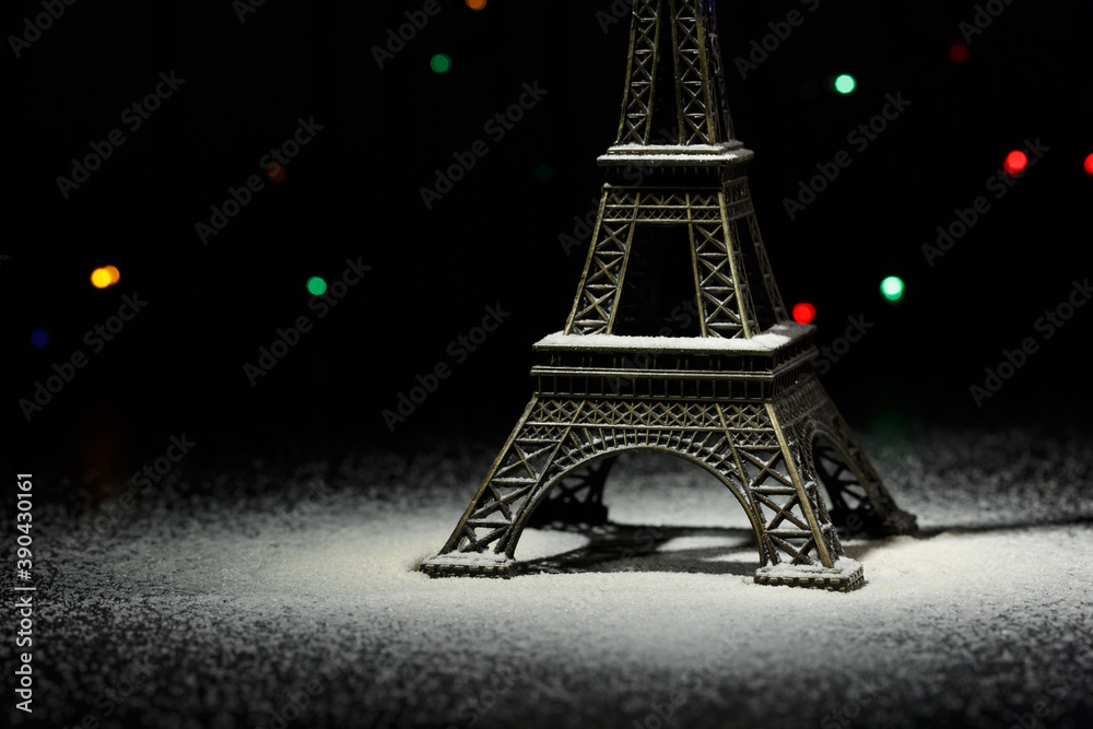 Miniature of the Eiffel Tower. Snow around the Eiffel Tower in Paris. In the dark - a ray of light from above and against the background of shining garlands. Eiffel Tower in the New Year. Macro. 