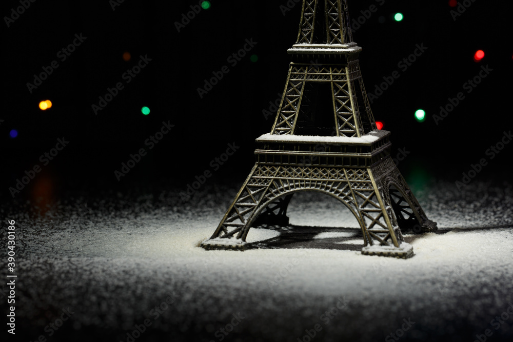 Miniature of the Eiffel Tower. Snow around the Eiffel Tower in Paris. In the dark - a ray of light from above and against the background of shining garlands. Eiffel Tower in the New Year. Macro. 