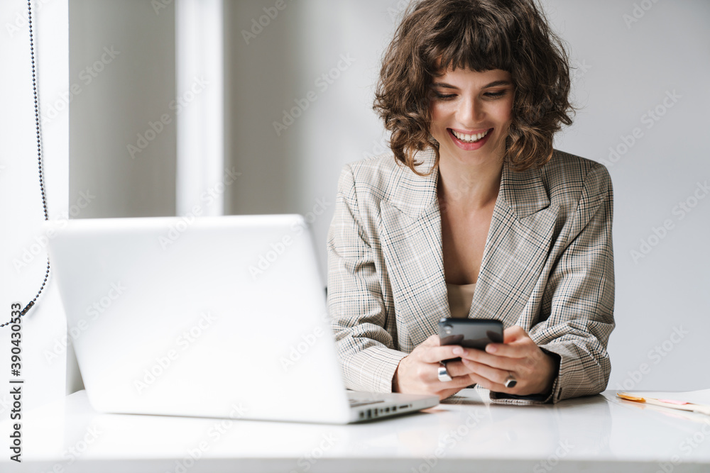 Joyful girl working with laptop and holding cellphone in office Joyful girl working with laptop and holding cellphone in office