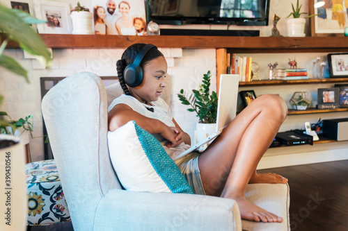 Girl in wireless headphones sitting in living room doing home school work on laptop