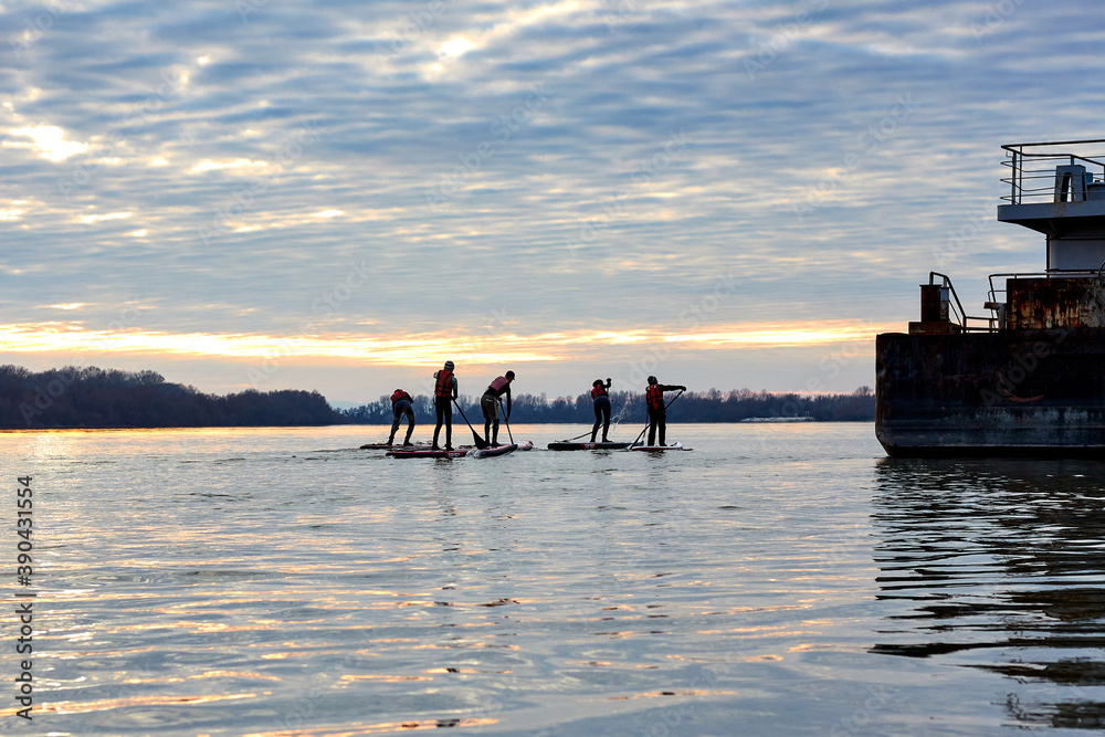 Children on SUP row in the winter Danube river at sunset