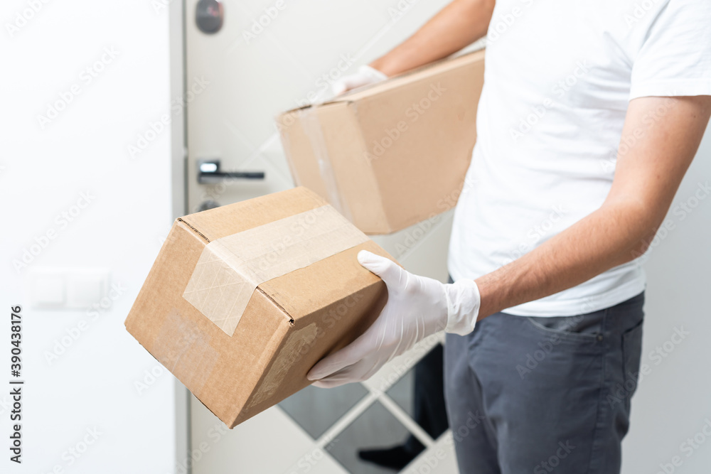 Courier, delivery man in medical latex gloves and mask safely delivers online purchases in white box to the door during the coronavirus epidemic, COVID-19. Stay home, safe concept. Courier, delivery man in medical latex gloves and mask safely delivers online purchases in white box to the door during the coronavirus epidemic, COVID-19. Stay home, safe concept.