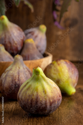 Close-up of wooden bowl with figs and purple gynura leaves, with selective focus, on wooden background, vertical photo