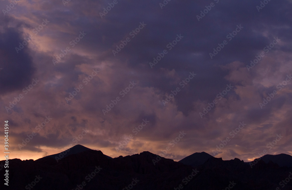 Magical sunset. View of the mountains silhouette at nightfall. Beautiful dusk purple and orange colors in the sky and clouds.