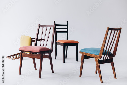 Four old wooden chairs with different colored seats stand empty on a white background  one chair inverted  selective focus