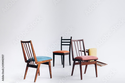Four old wooden chairs with different colored seats stand empty on a white background, one chair inverted, selective focus