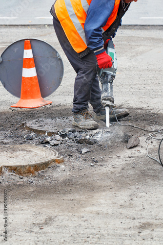 A worker repairs a section of the road with an electric jackhammer.