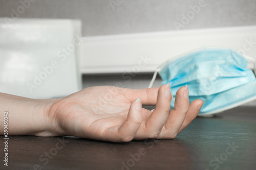 An inanimate female hand lies on a table made of dark wood by a blue protective facial mask
