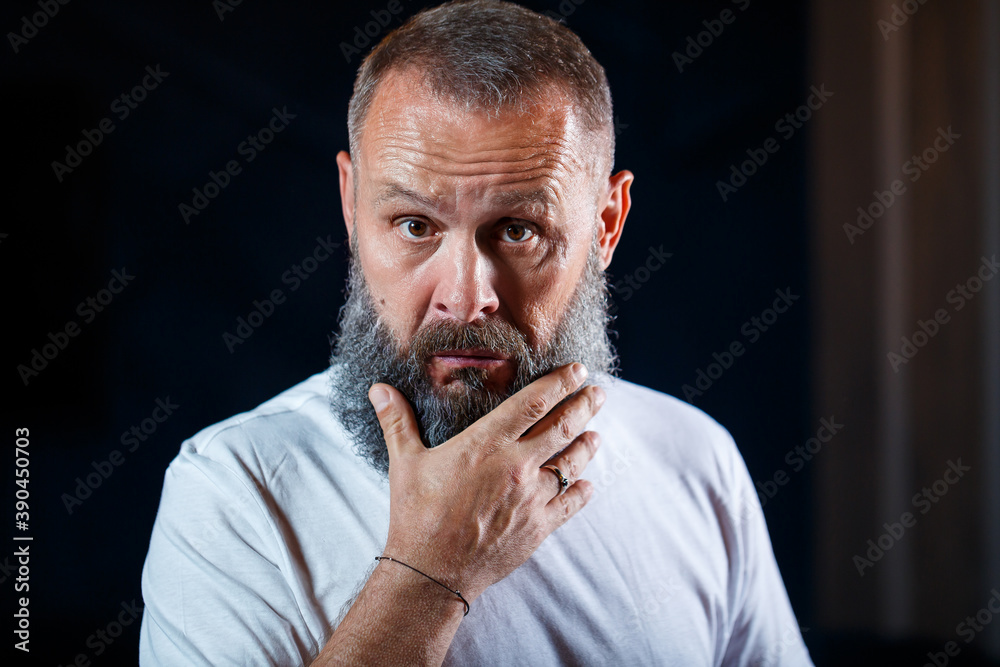 Emotional portrait of an adult gray-haired man with a beard in a white t-shirt Emotional portrait of an adult gray-haired man with a beard in a white t-shirt