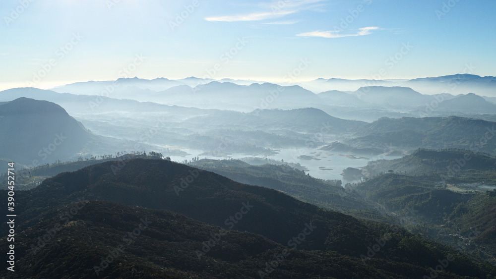 Sunlit valley view in the morning. Panoramic  view from Adams Peak or Sri Pada. Fresh foggy mountains landscape mostly in soft blue color tones. Sri Lanka.