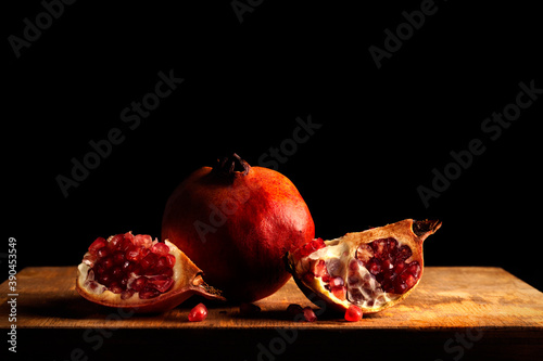 Still life with a whole pomegranate and two quarters on a wood and dark background in baroque style photo