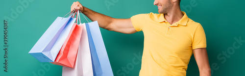 cropped view of cheerful delivery man carrying shopping bags on blue, banner