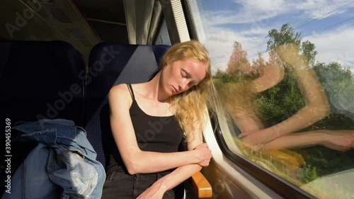 Beautiful woman falls asleep in the train. Female sleeps while having train trip home after work. Scandinavian look, freckles, blond hair, sunny evening.