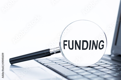 Funding word written on a magnifier that lies on the laptop keyboard, business concept