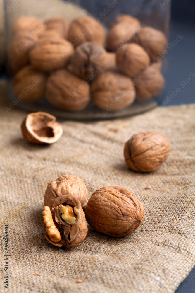 close-up three walnuts. unpeeled and peeled walnuts in shells on a black table and in a glass jar. brown nuts with sackcloth on a dark background. copy space. dried walnut and fruit. vertical close-up three walnuts. unpeeled and peeled walnuts in shells on a black table and in a glass jar. brown nuts with sackcloth on a dark background. copy space. dried walnut and fruit. vertical