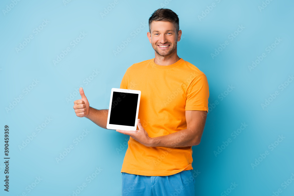 happy man in t-shirt holding digital tablet with blank screen and showing thumb up on blue happy man in t-shirt holding digital tablet with blank screen and showing thumb up on blue