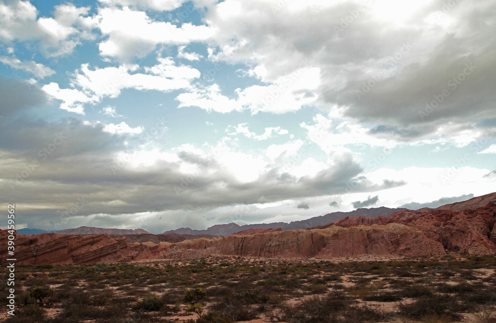 Geology. View of the sandstone and red rocky formation and mountains in the arid desert under a cloudy sky.