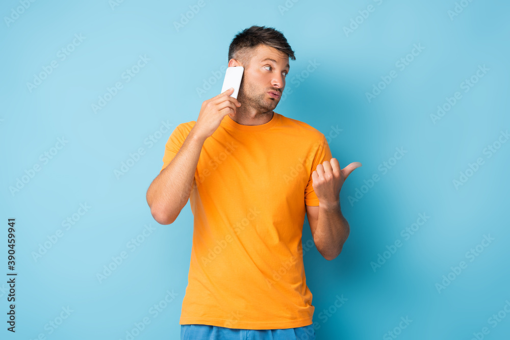 man in t-shirt talking on smartphone and pointing with thumb on blue man in t-shirt talking on smartphone and pointing with thumb on blue
