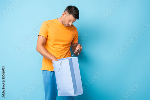 surprised man in t-shirt looking at shopping bag on blue